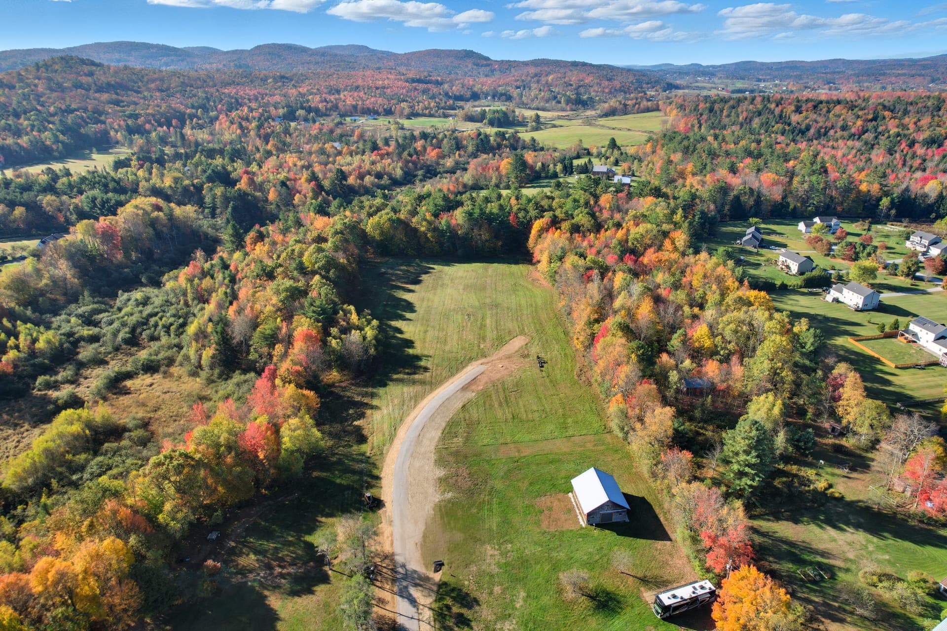 Aerial of a cleared building lot and new road bordered by bright fall forest