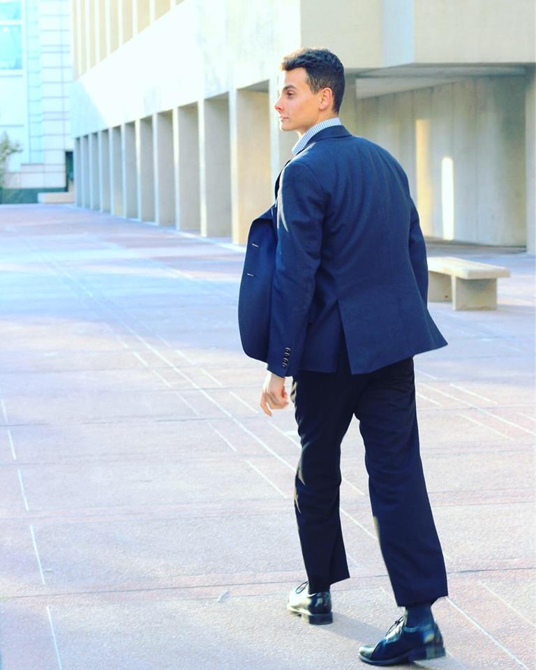 Lifestyle branding portrait of a man in a navy suit walking through a modern plaza