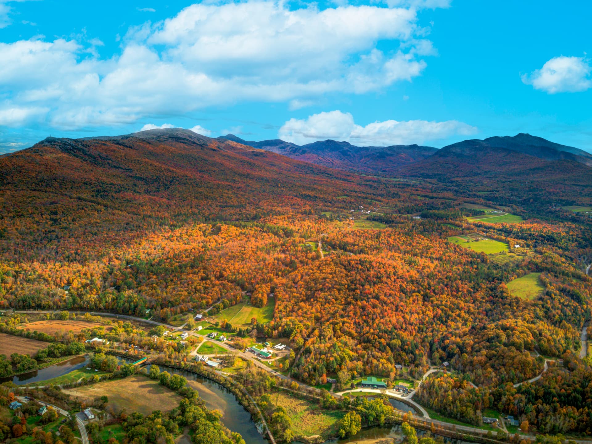 Wide aerial of a river valley and village surrounded by peak autumn color