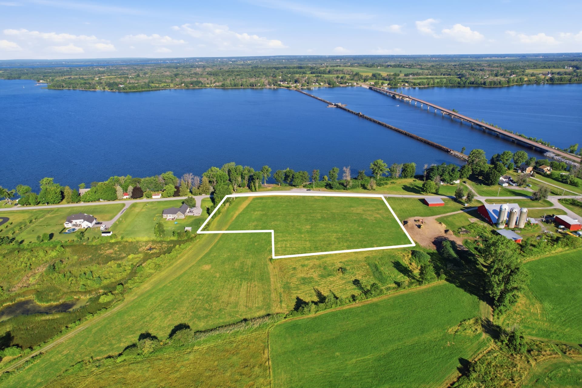 Aerial of a marked parcel near a long lake crossing bridge and farm fields