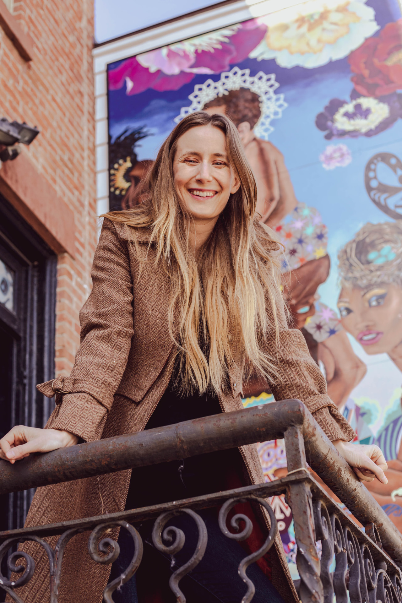 Lifestyle branding portrait of a smiling woman on a balcony in front of a colorful mural