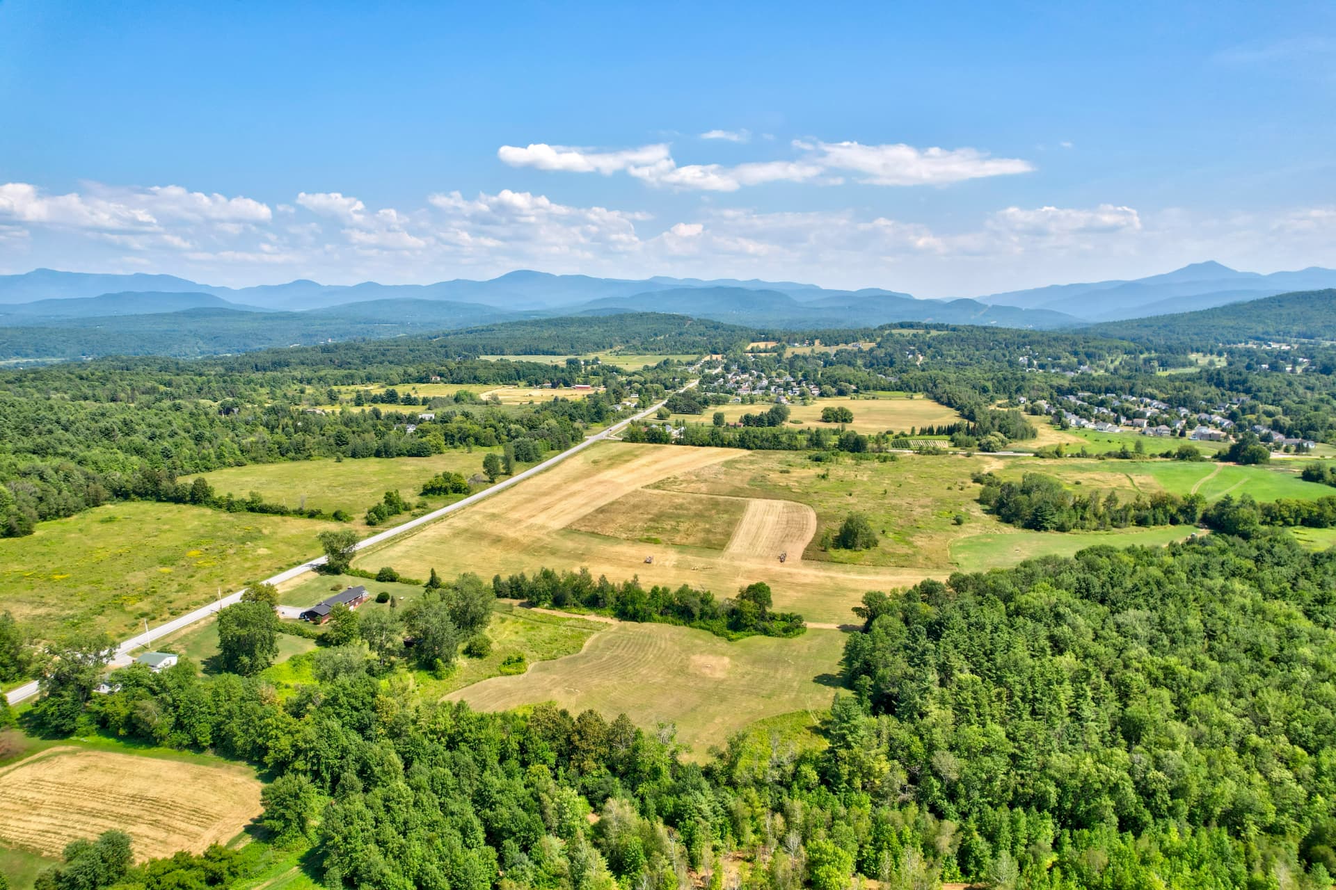 Summer aerial over open farmland and hayfields with layered blue mountains