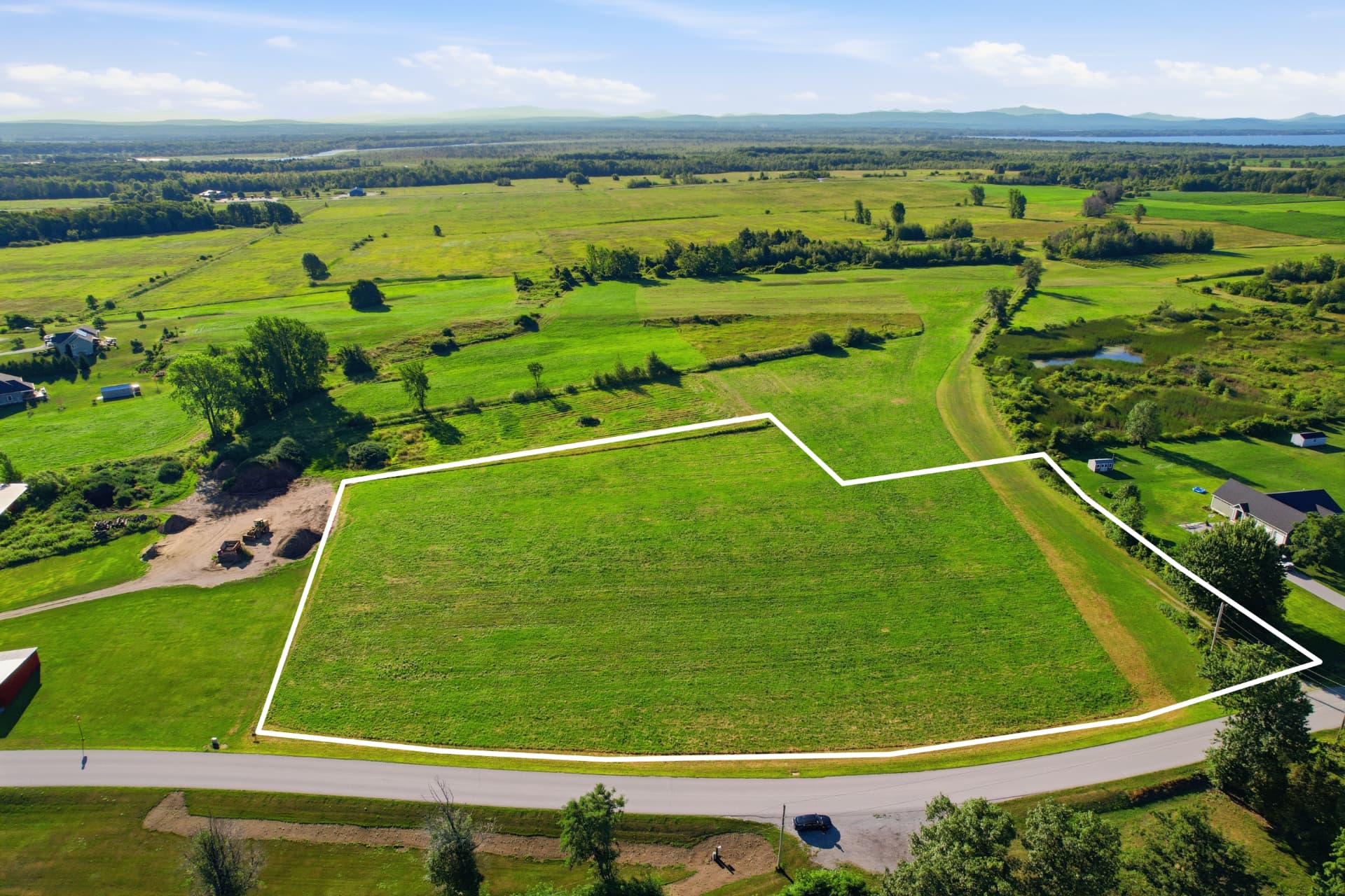 Aerial of a surveyed green lot outlined in white with lake and farmland beyond