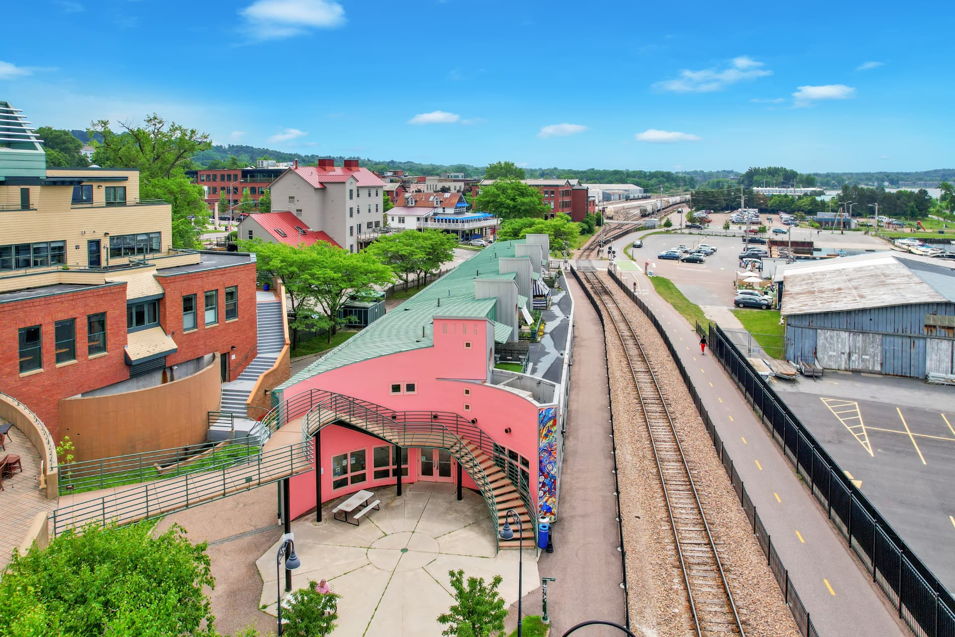 Aerial view of a pink waterfront building beside railway tracks and marina