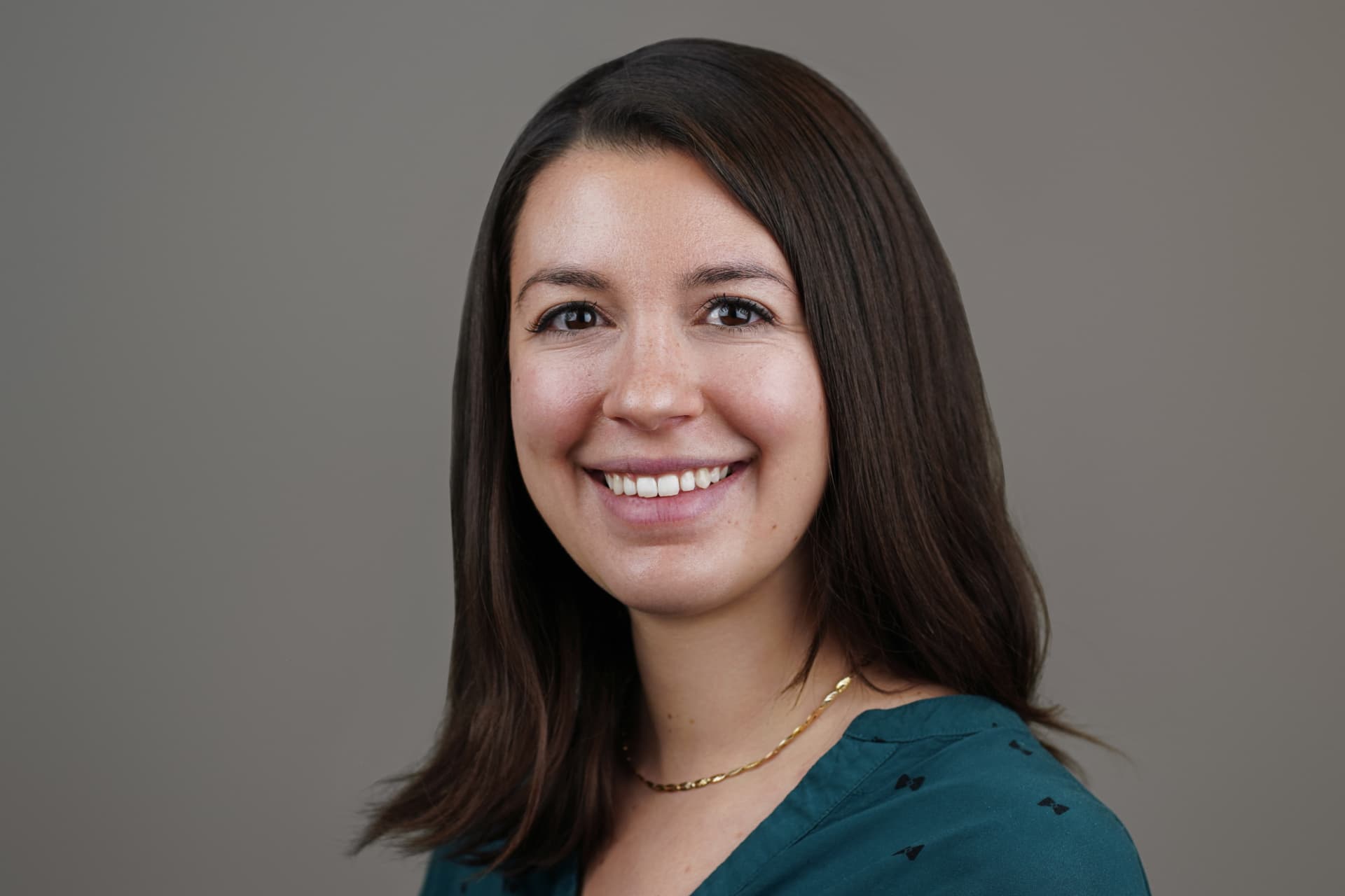 Studio headshot of a smiling professional against a neutral gray backdrop