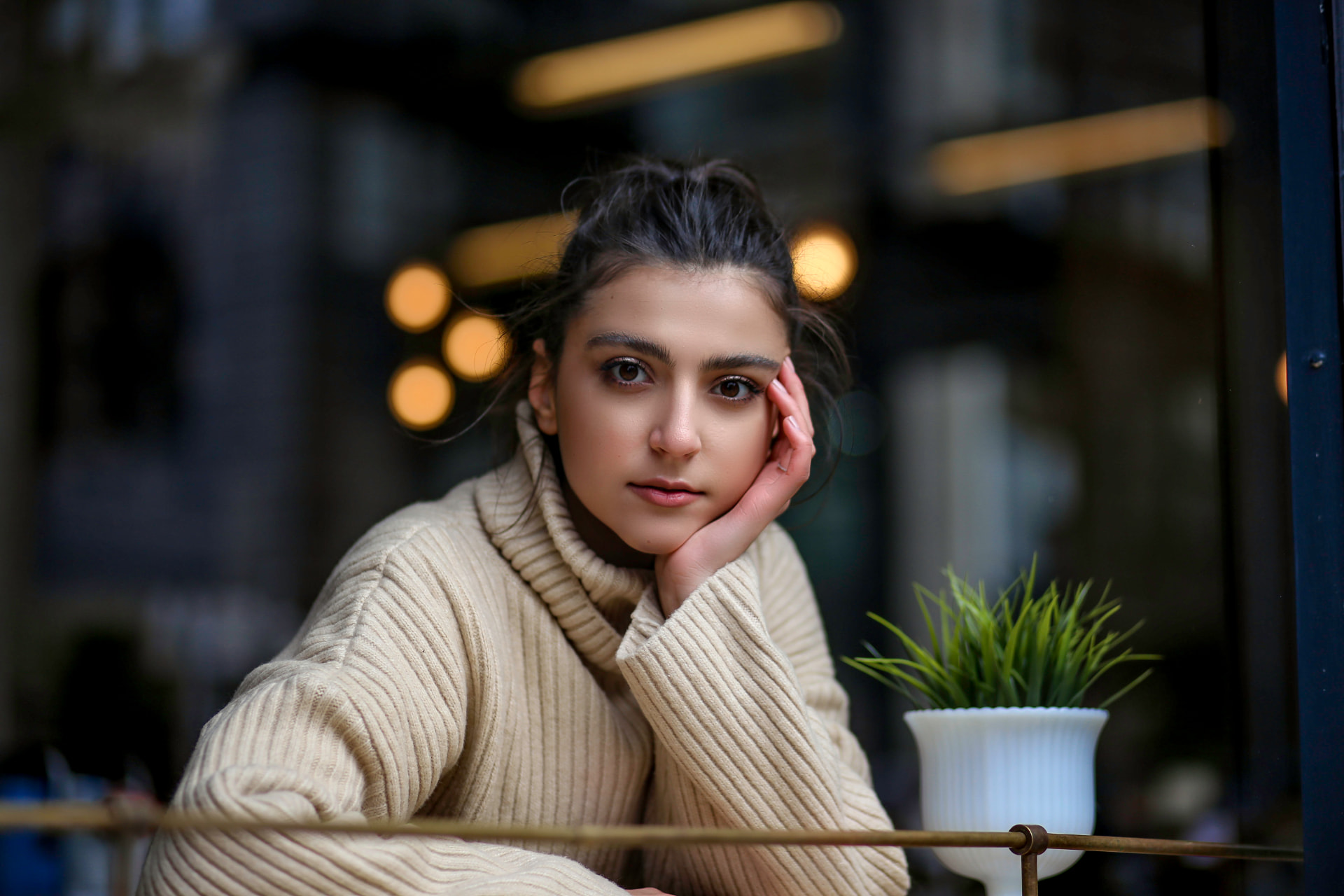Lifestyle portrait of a young woman in a cream turtleneck at a cafe window