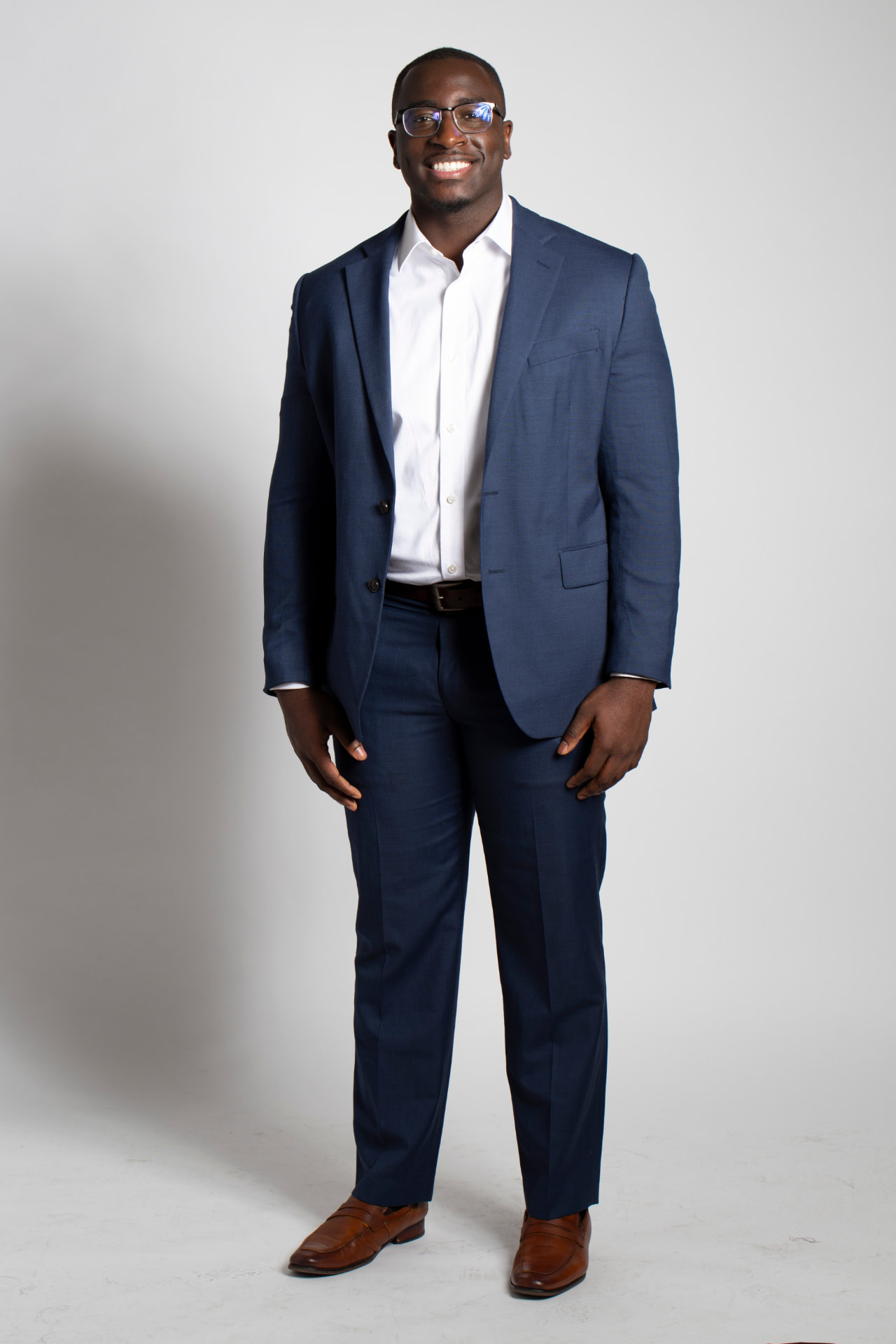 Full-length branding portrait of a smiling man in a navy suit against a white backdrop