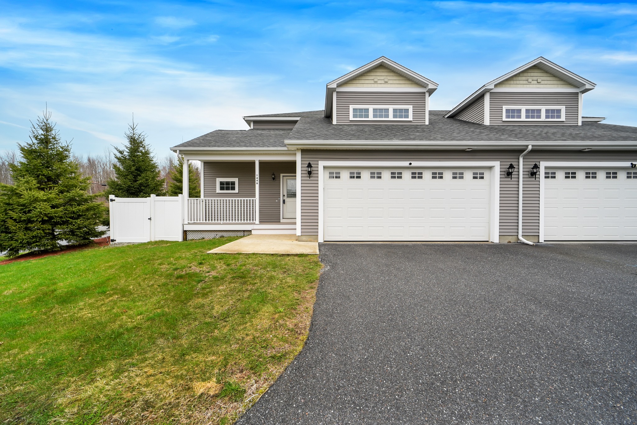 Light gray home with dormer windows, a covered porch and a wide attached garage at the end of a paved driveway.