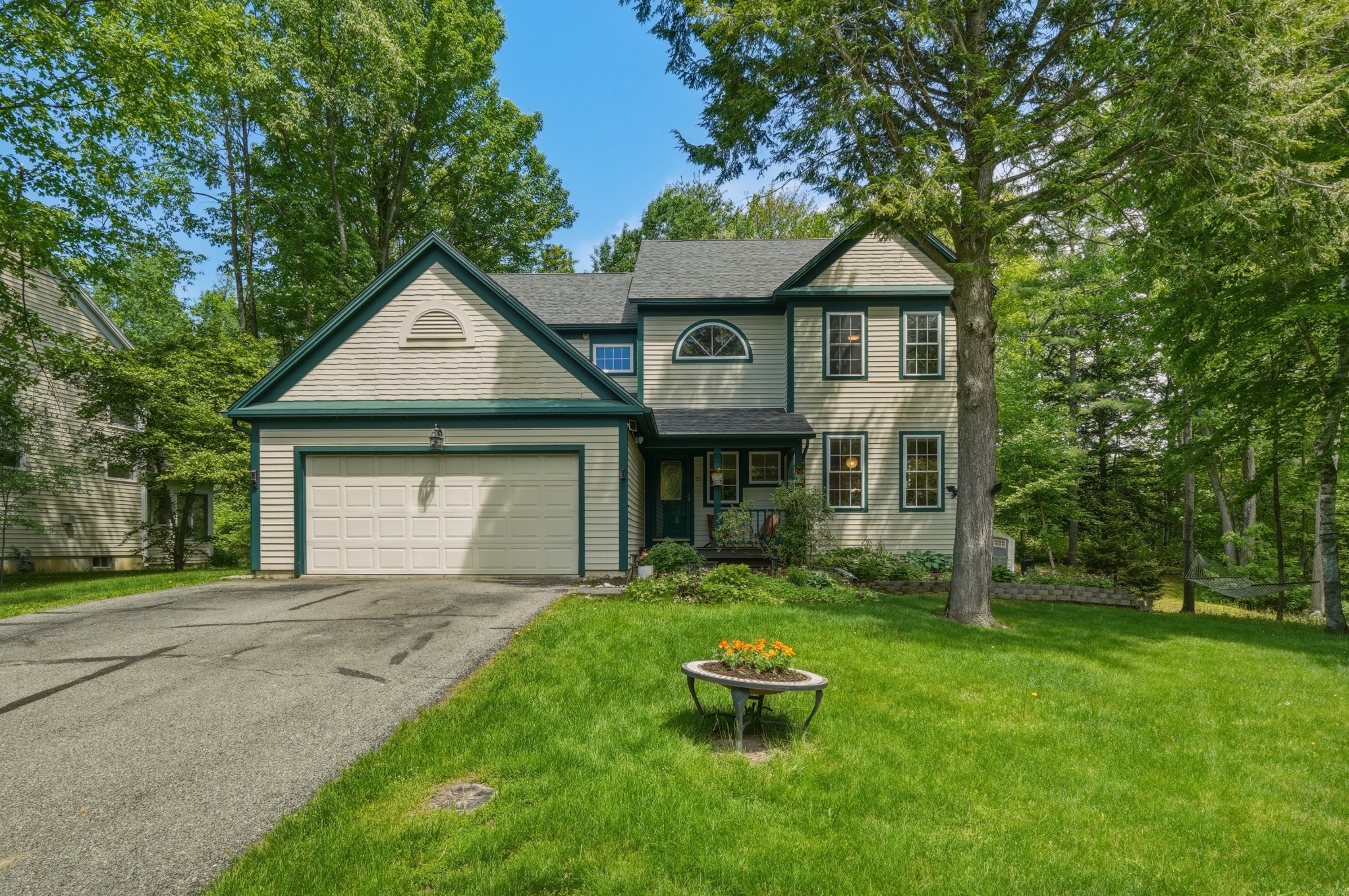 Two-story colonial home with a green garage door and trim, framed by tall mature trees over a mown lawn and driveway.