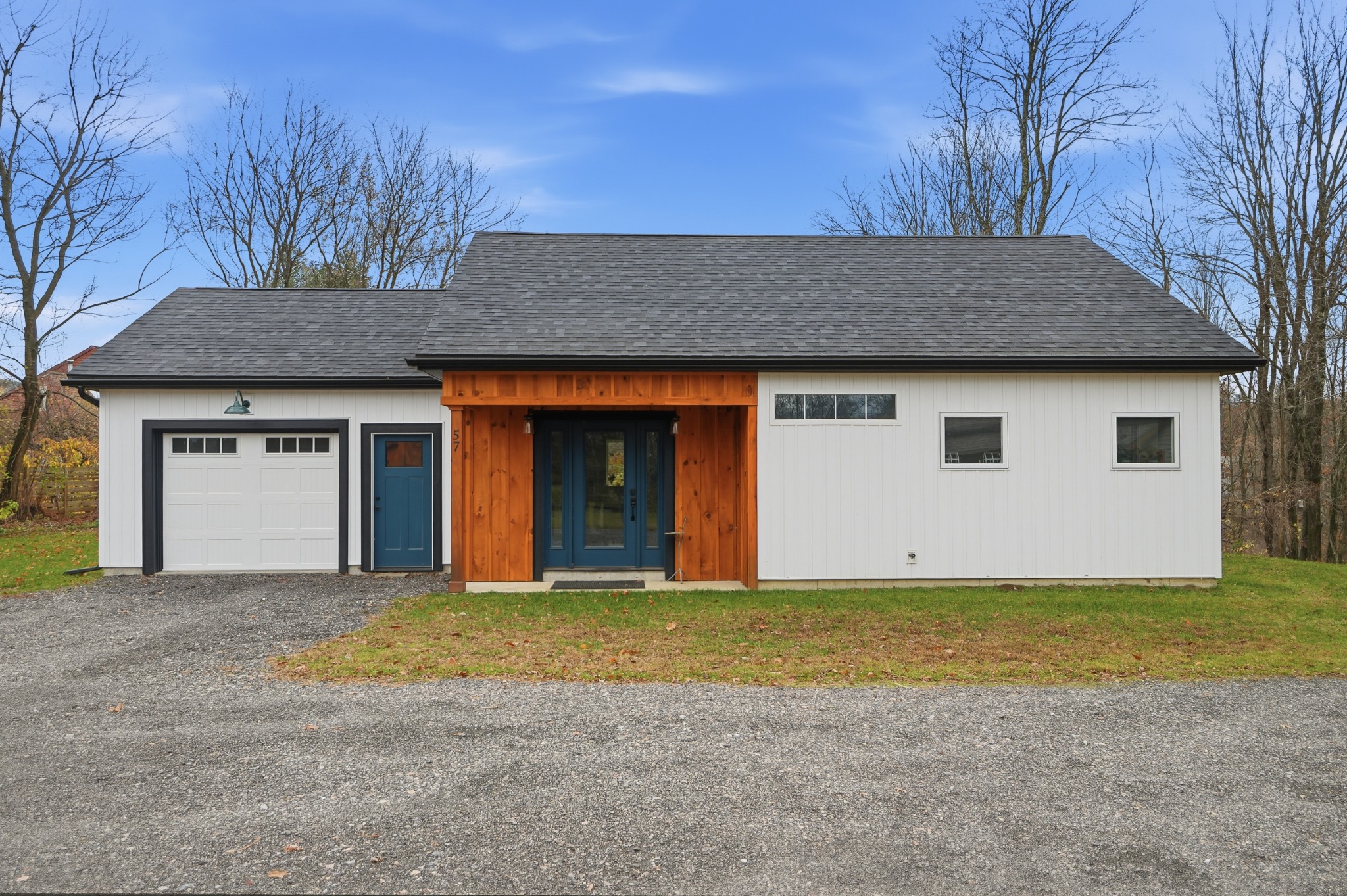 Single-story white outbuilding with a garage bay and a vertical wood-clad entry section beside a gravel apron.