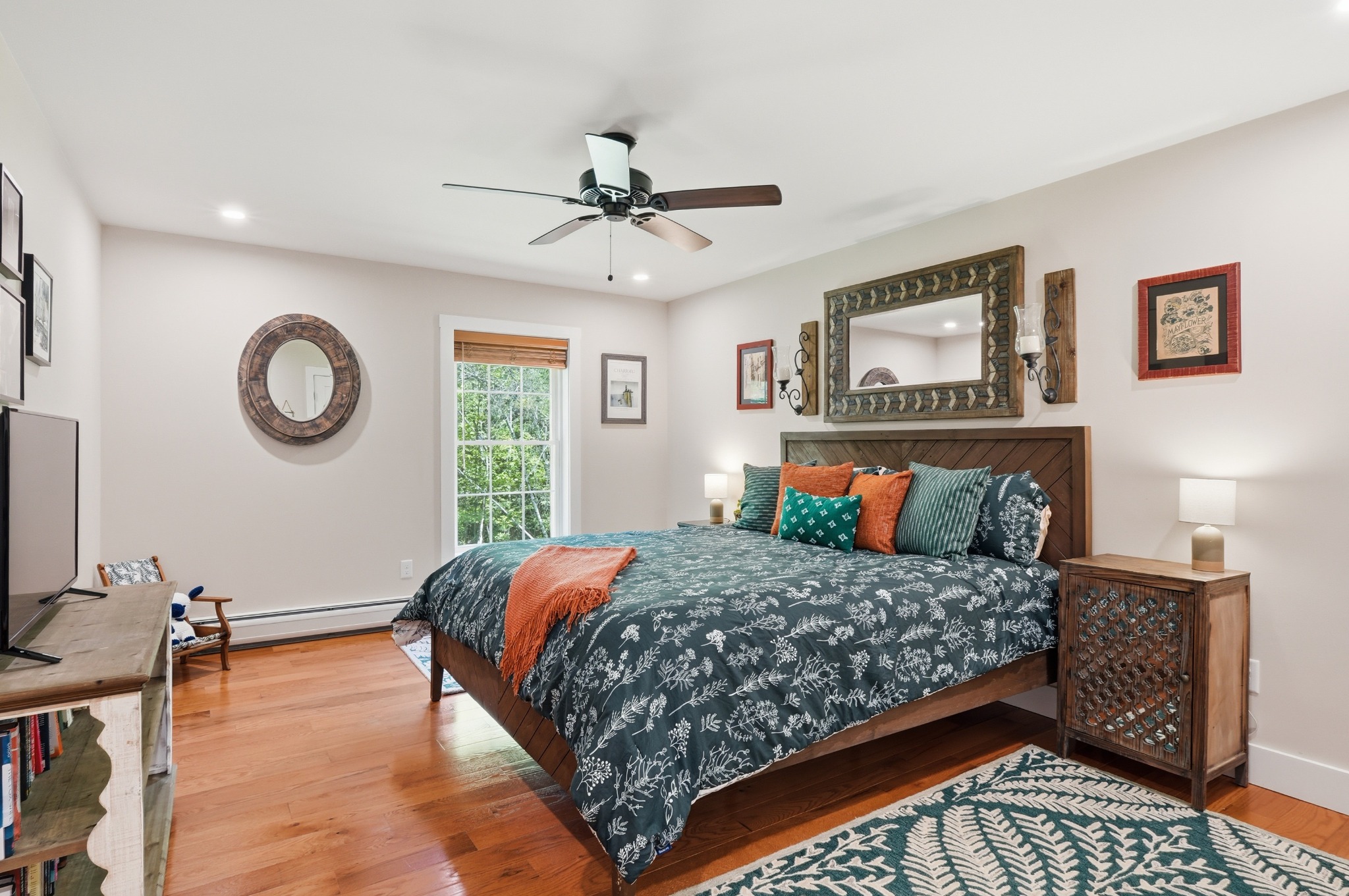 Bedroom with a carved wood headboard, teal patterned bedding, framed mirrors and artwork, and a ceiling fan overhead.