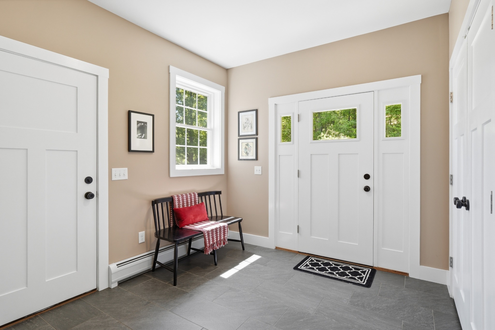 Tiled entry foyer with a white paneled front door, sidelight windows, a small bench and framed photographs on the wall.