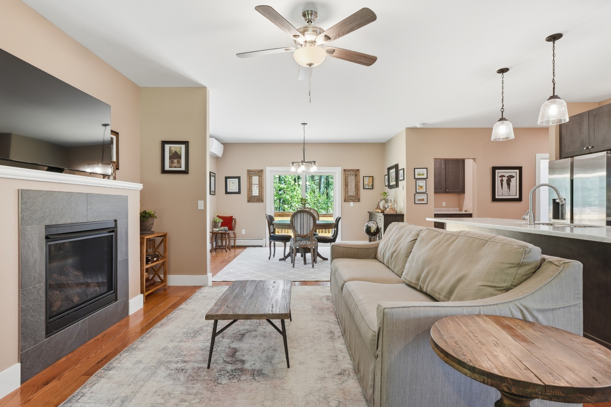 Living room with a tiled gas fireplace, sectional sofa and ceiling fan, opening through to a dining table and kitchen counter.