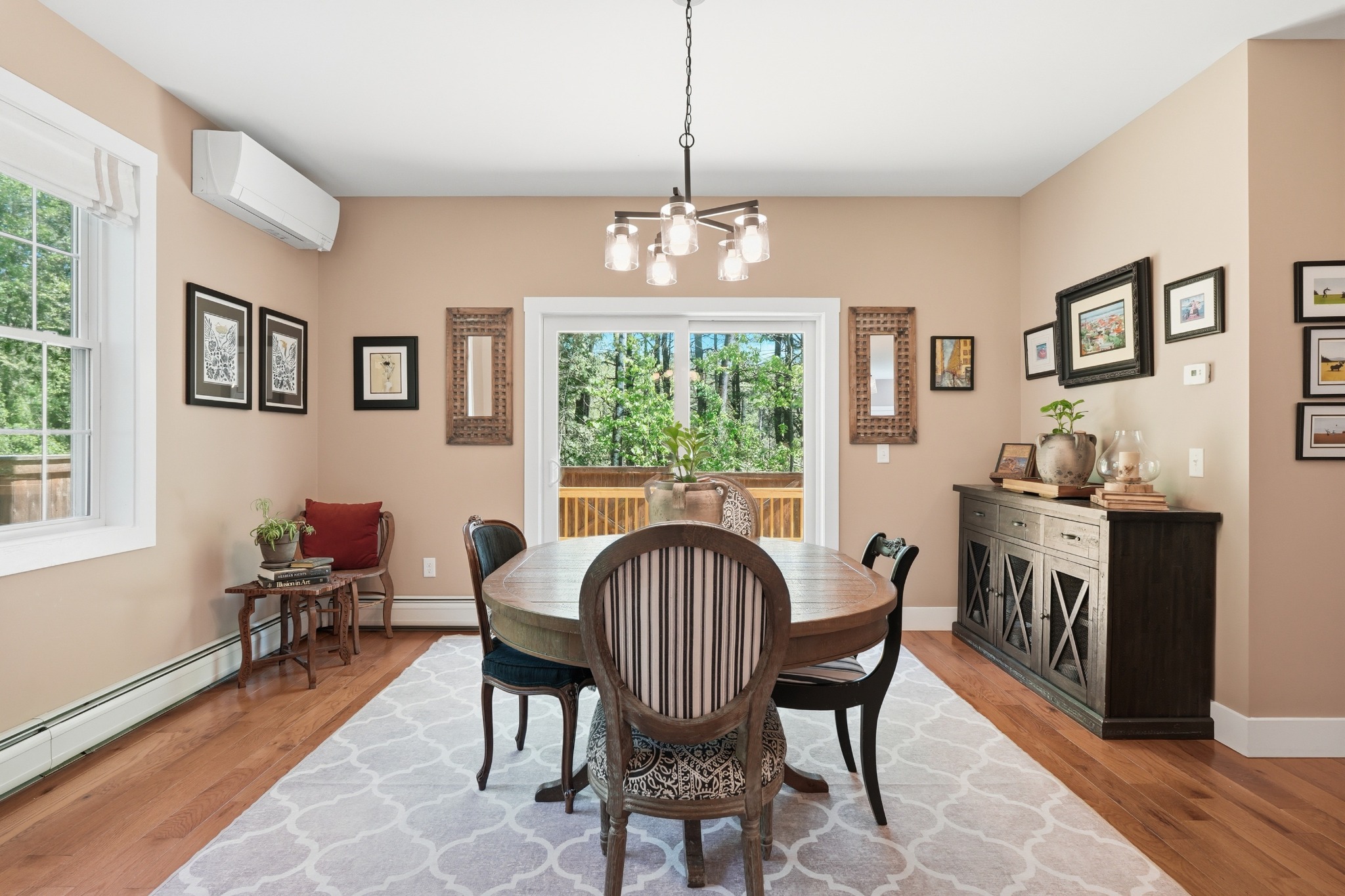 Dining room with a round wood table and spindle chairs on a patterned rug, warm peach walls and a bay window to the deck.