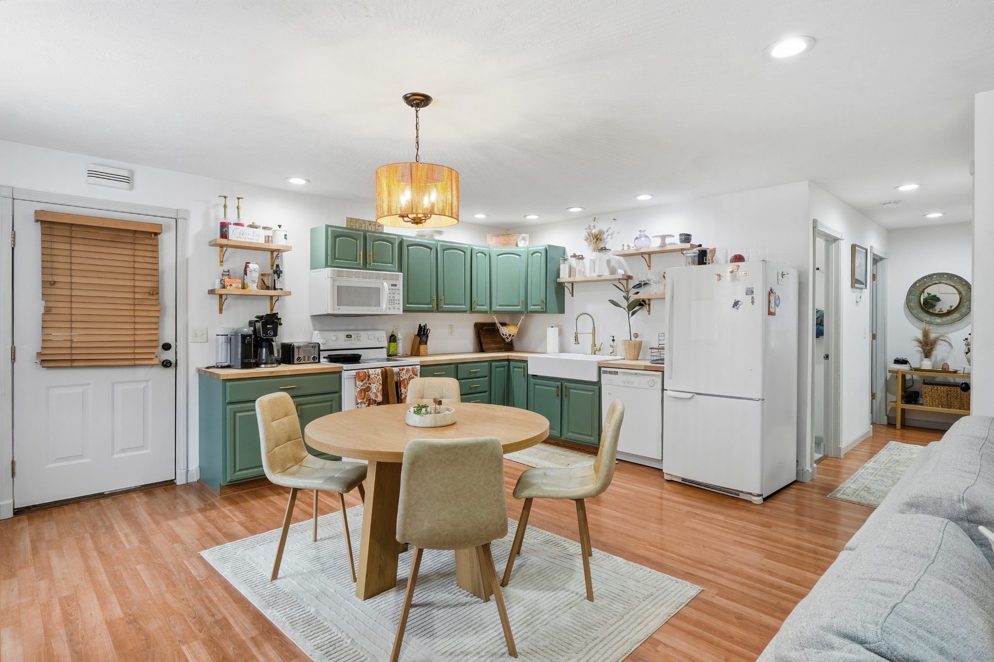 Eat-in kitchen with green cabinets, a farmhouse sink, white appliances and a round table with wood chairs on a light rug.